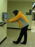 A photograph shows awkward posture of a tall student standing at a too low computer kiosk.